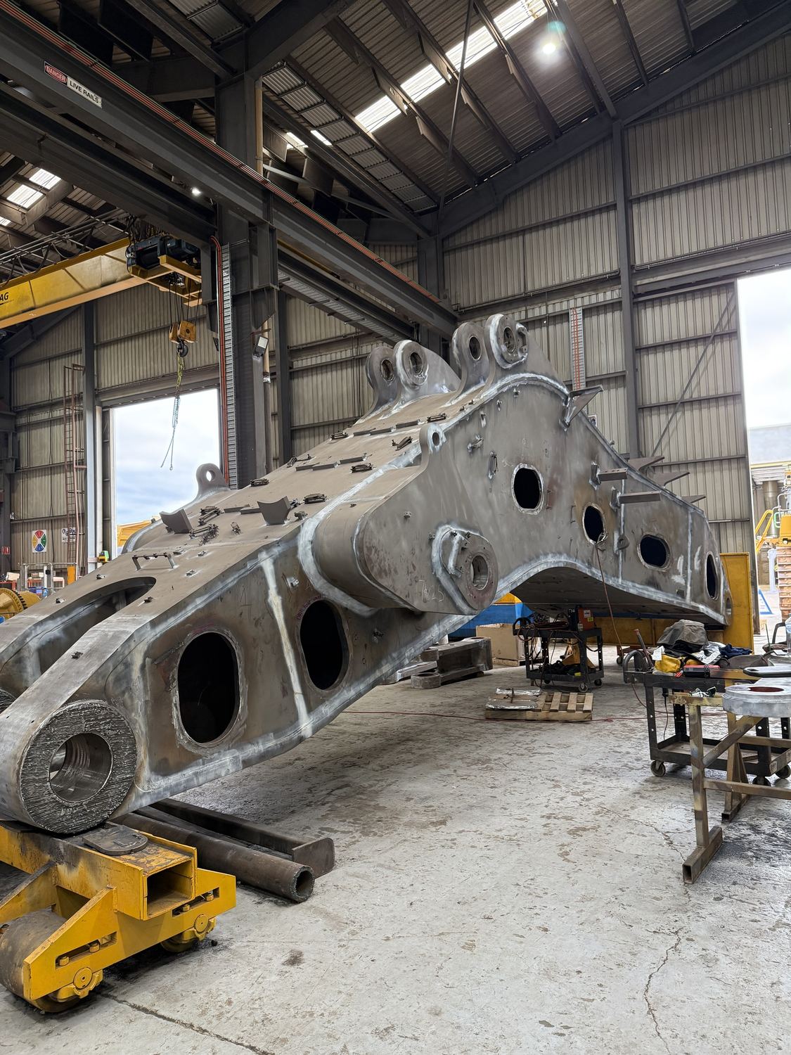 Excavator boom and stick supported on stands in the workshop during a crack-repair rebuild